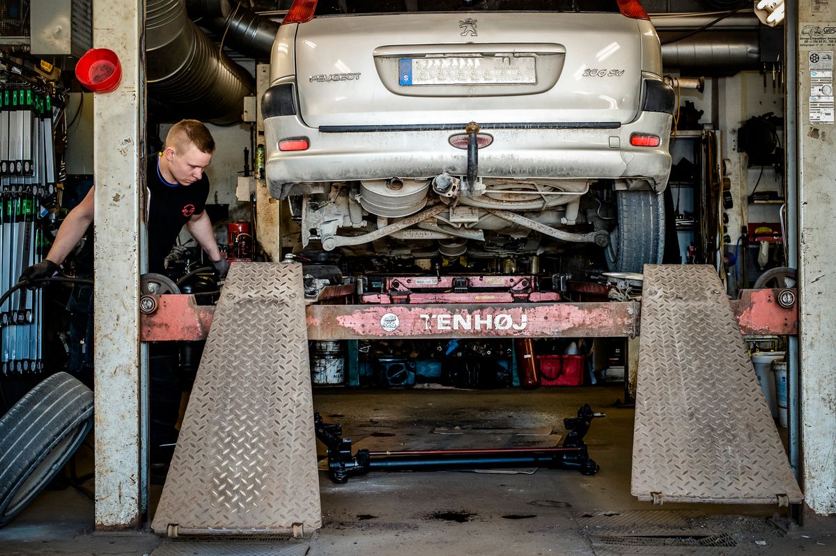 Mekaniker i arbete inne i verkstaden. Arbetar med bil upphissad på bilhiss.